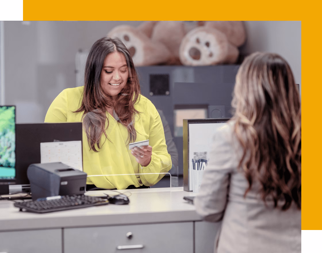 Credit union employee assisting a member with account services while reviewing secure digital banking systems and payment information on a computer workstation. Showing DataYard offering scalable and secure cloud hosting for credit union websites and applications